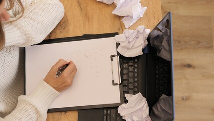 Woman crumples paper while working at desk struggling with new idea. Frustration shows as another idea is discarded, capturing creative process. Perfect for themes of brainstorming and idea generation