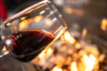 A delicate wine glass filled with dark red wine rests in front of crackling flames. Ideal for seasonal campaigns focused on warmth and indulgence. Great for lifestyle blogs and winter-themed ads.