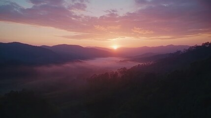 Obraz premium A panoramic view of a misty valley at sunset with a golden light shining over the mountains.