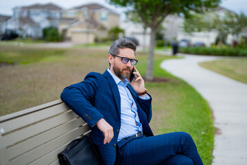 Freelance. Businessman freelancer in suit sitting on bench. Portrait of freelancer on park bench outdoors. Freelancer thinking about business. Freelancer work on laptop on neighborhood. Free business.