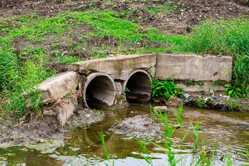 A dirty, muddy ditch with two pipes coming out of it
