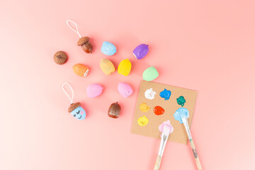 Hand painted acorns with emoji faces next to unpainted acorns, paint palette, and brushes on pink...