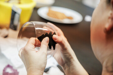 A child Cristmas Craft  a holiday decoration by applying a black felt shape to a glass at a cozy indoor table during the festive season