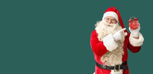 Santa Claus pointing at alarm clock on green background with space for text