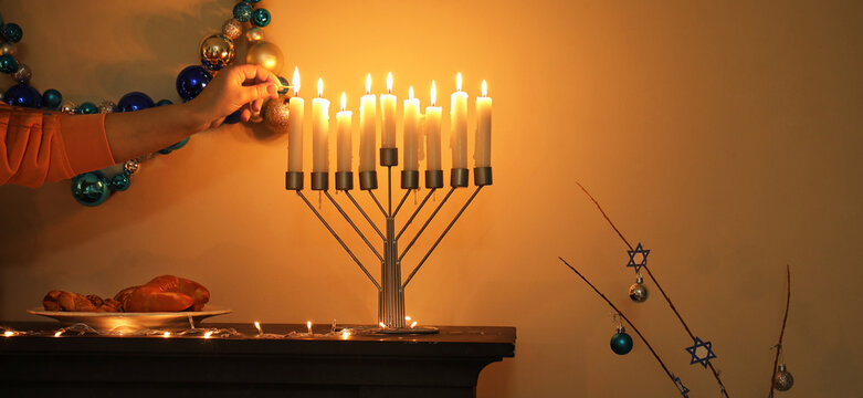 Woman lighting menorah candles on mantelpiece at evening. Hanukkah celebration
