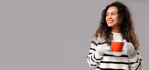Happy young African-American woman holding mug of hot mulled wine on grey background with space for...