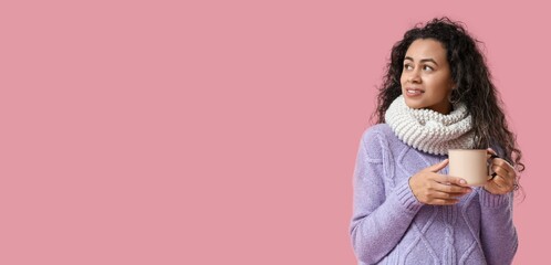 Young African-American woman holding mug of hot mulled wine on pink background with space for text