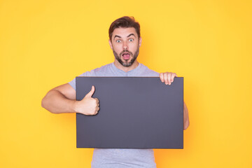 Handsome man holding empty board and pointing finger on board. Guy showing blank board with...