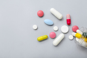 Overturned bottle with different pills on grey background