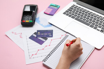 Female hand with credit cards, laptop, charts and notebook on pink background. House rent concept