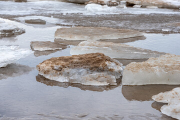 Melting ice patches reveal rocky shoreline at low tide in a quiet coastal area during early spring