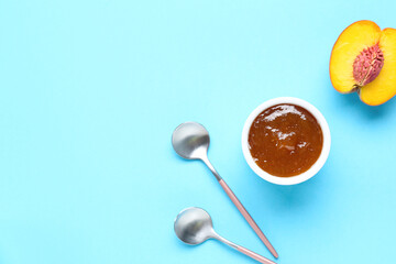 Bowl of sweet peach jam and spoons on color background