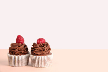 Tasty chocolate cupcakes with raspberries on beige background