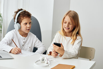 Obraz premium Happy Caucasian children studying online at home, using laptops and tablets They are sitting at a table in the living room, wearing headphones and focused on their screens The background shows a cozy