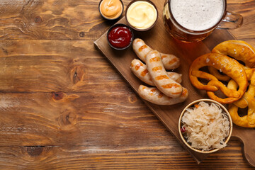 Tasty Bavarian sausages, sauces, sauerkraut, pretzels and mug of beer on wooden background. Oktoberfest celebration