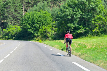 Fototapeta premium Alone unrecognizable cyclist rides his bicycle along a road in natural scenery on french alps