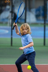 Child boy playing tennis on court. Blonde little boy hit tennis ball with tennis racket. Active exercise for kids. Summer activities for children. Child learning to play tennis. Sport Kid hitting Ball