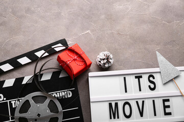 Movie clapper with text ITS MOVIE TIME,  film reel and Christmas decor on grey grunge background