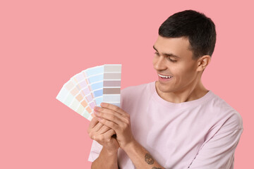 Young man with paint palettes on pink background