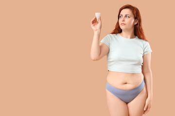 Young woman in period panties holding menstrual cup on beige background