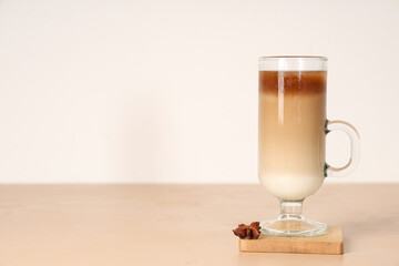 Glass cup of iced latte and star anise on beige table