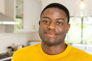 Fototapeta premium Smiling African american man in yellow sweater enjoying cozy holiday moment at home