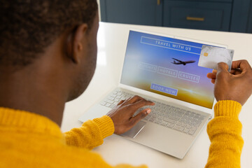 African american man booking holiday online using laptop and credit card at home