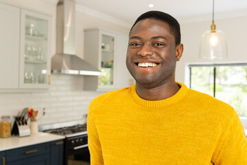 Smiling African american man in yellow sweater enjoying time at home in modern kitchen