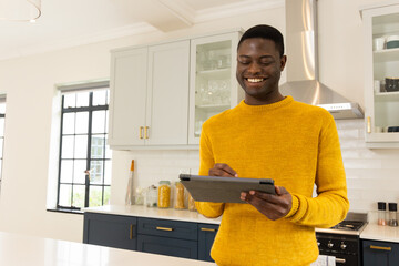 Smiling African american man in kitchen using tablet, enjoying holiday preparations at home