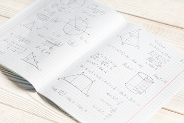 Copybook with handwritten maths formulas on white wooden background