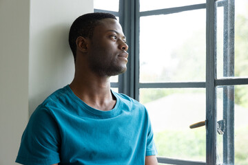 African American man gazing out window, reflecting peacefully at home