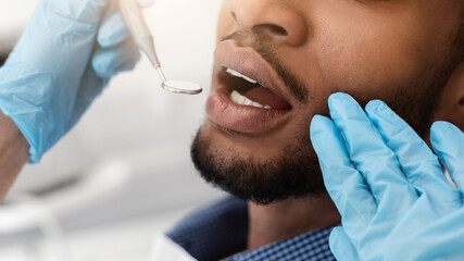Cropped of dentist hands in gloves checking black man mouth with tools