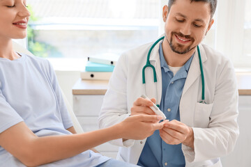 Male endocrinologist measuring blood sugar level of young woman in clinic