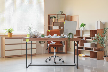 Interior of messy office with workplace, plants and shelf units