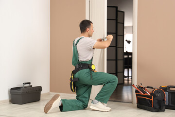 Male worker with screwdriver repairing door at home