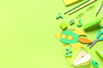 Different school stationery and paper rocket on green background
