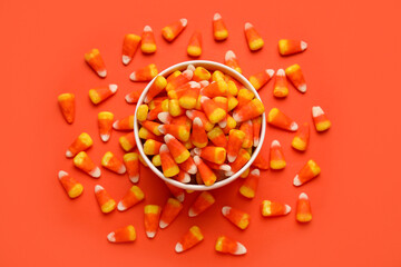 Bowl of tasty Halloween candy corns on orange background