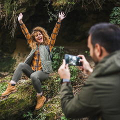 husband take a photo of wife backpacker in front cave in the forest