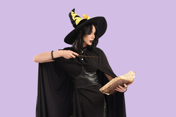 Beautiful young woman dressed as witch for Halloween with magic wand and spell book on purple...