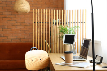 Modern workplace with laptop, cup of coffee and folding screen near window