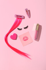Composition with false eyelashes, hair strand, lipstick and clips on pink background