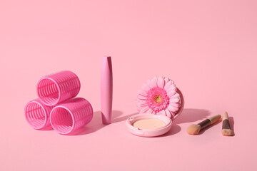 Decorative cosmetics, makeup brushes and hair curlers on pink background
