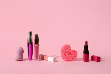 Composition with different lipsticks and makeup sponge on pink background