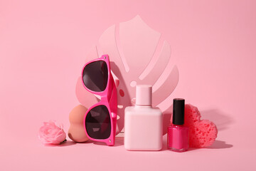 Composition with perfume, nail polish, sunglasses and makeup sponge on pink background