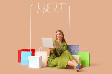 Beautiful young happy woman with shopping bags, laptop and empty rack sitting on beige background