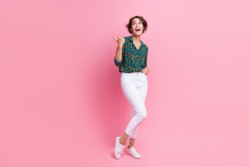 Full length photo of impressed woman wear print blouse white trousers directing look at sale empty space isolated on pink color background