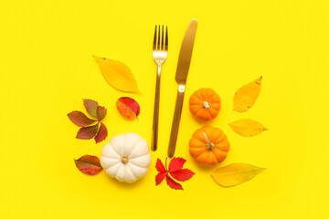Stylish cutlery with fresh pumpkins and autumn leaves on yellow background