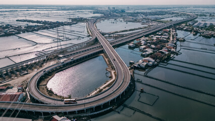 A toll road curves through a vast expanse of floating fish farms, with kerambas scattered across the calm water beneath the highway.