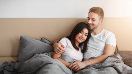 Loving Diverse Couple Hugging Lying In Bed Enjoying Weekend Together. Happy Marriage And Sex Life Concept.