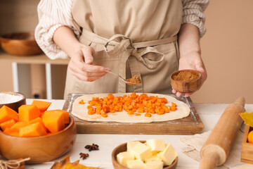 Woman preparing tasty pumpkin strudel on table in kitchen